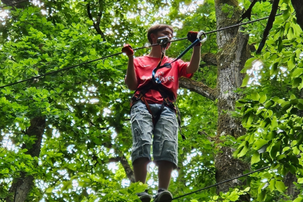 Orphelin d'Orphéopolis en harnais suspendue dans les arbres lors d’un parcours accrobranche