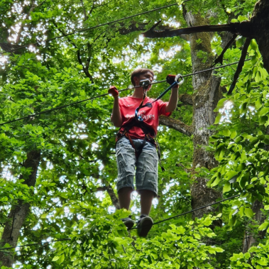 Orphelin d'Orphéopolis en harnais suspendue dans les arbres lors d’un parcours accrobranche