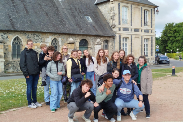 Orphelins d'Orpéopolis posant ensemble à l'extérieur devant un bâtiment ancien en pierre avec des fenêtres gothiques et un toit gris. Certains des jeunes sont debout, d'autres accroupis devant, et tous semblent heureux et détendus. C'est une journée ensol