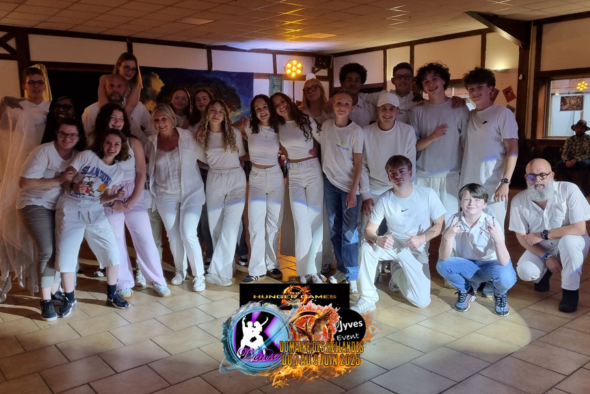 Orphelins d'Orpéopolis posant pour une photo dans une salle aux lumières tamisées. La plupart portent des vêtements blancs ou clairs. Ils sourient et semblent heureux. Au centre de l'image, un logo coloré avec une guitare et du feu indique 