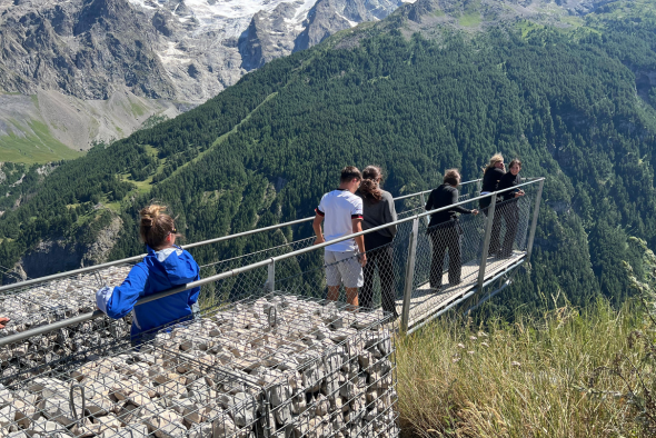 Orphelins d'Orphéopolis marchant sur une passerelle suspendue au-dessus d’une vallée verdoyante.
