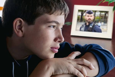 un jeune garçon est adossé sur un bureau le regard dans le vide. A côté de lui, une photo est encadrée d'un homme en uniforme de police. 